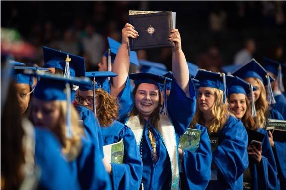 Student proudly holding diploma above her head after graduating from Grand Valley